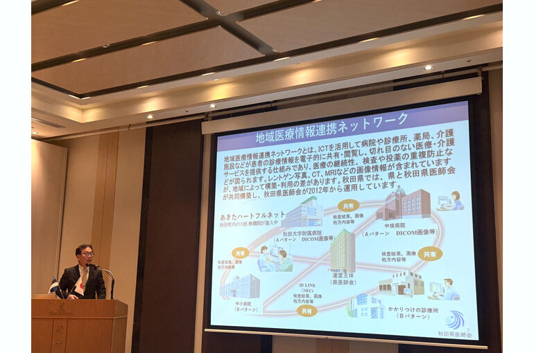   秋田キャッスルホテルで島田薫秋田県議会副議長がスマートグラスとスマートリングを着用し、秋田県の医療DXについて講演する様子    